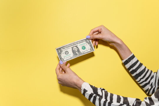Hands holding US dollar bill on yellow background, close-up