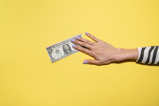 Hand reaching for US dollar bill on bright yellow background