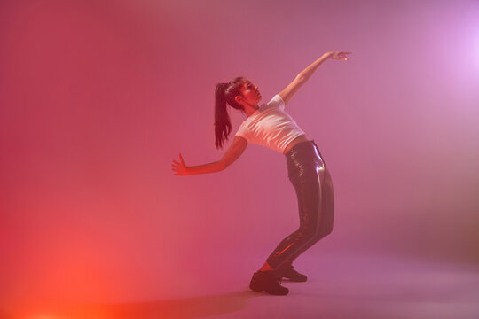 Woman dancer performing modern move in pink studio light