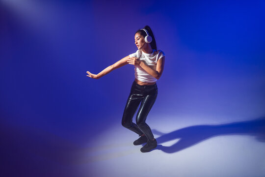Woman dancer in headphones dancing in blue studio light