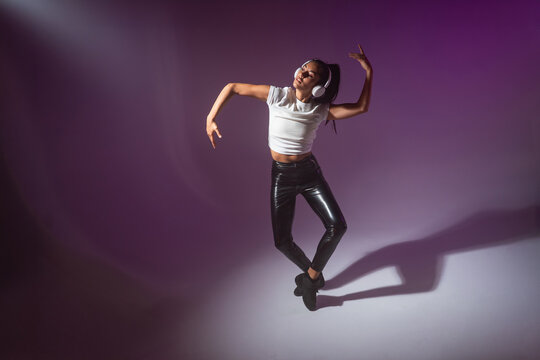 Young woman dancer in headphones moving to music in studio
