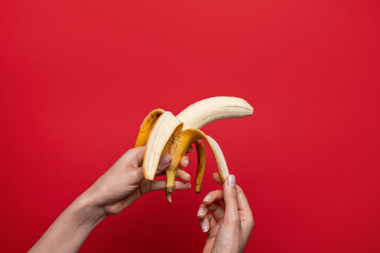 Woman hand peeling banana on red background, sex concept