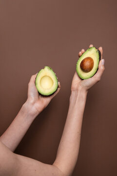 Hands holding halved avocado on brown background, closeup