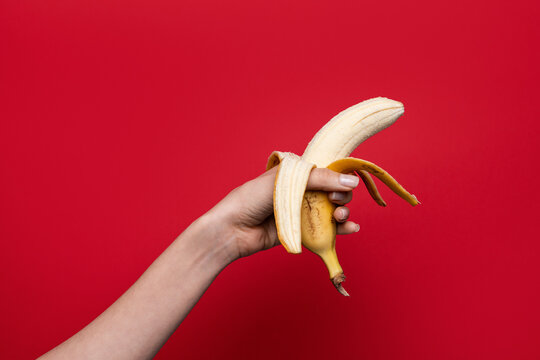 Hand holding peeled banana on red backdrop, sex concept