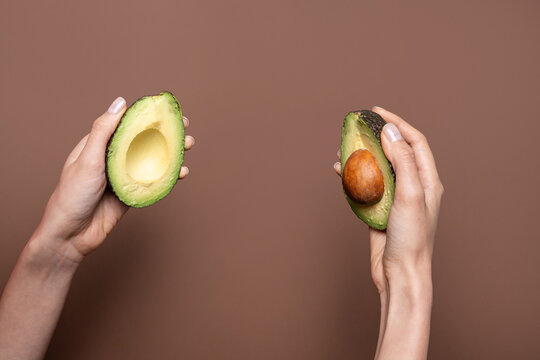 Hands holding avocado halves on brown background with copy space
