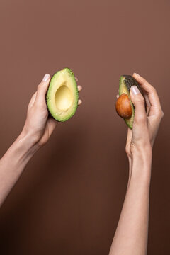 Hands holding avocado halves on brown background, closeup