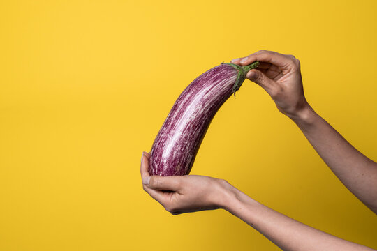 Hands holding eggplant on yellow background, sex concept