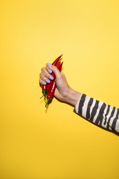 Hand holding red chili pepper on bright yellow backdrop