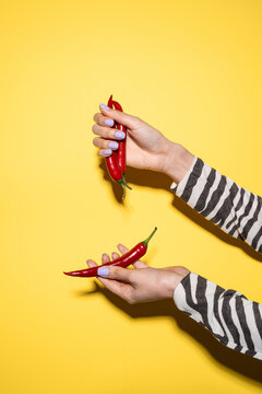 Hand holding red chili pepper on yellow background