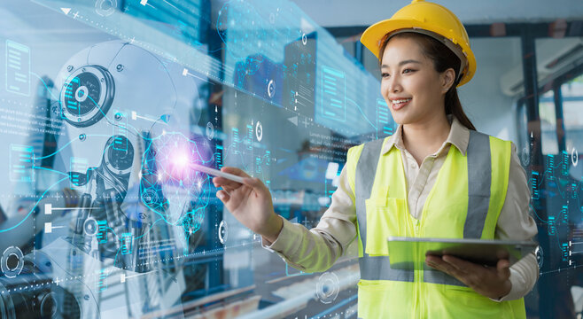 A female industrial engineer wearing a safety helmet using a tablet to analyze digital data on a futuristic screen, representing smart industry, artificial intelligence and data management.