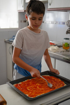 A child spreading tomato over pizza dough
