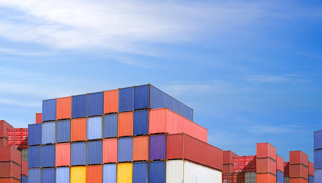 Stack of colorful cargo containers in logistics yard against blue sky background. Global business trade, industrial shipping, international transport, import export hub and commercial economy concept