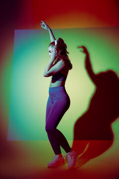 Young woman dancer posing in studio with colored light