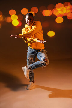 Urban street dancer in orange hoodie under bokeh lights