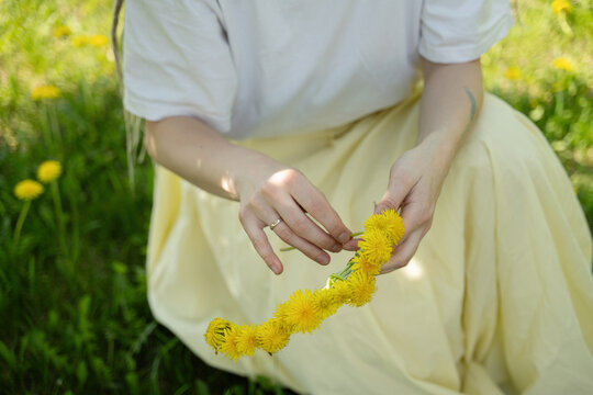 Woman making dandelion chain in summer park
