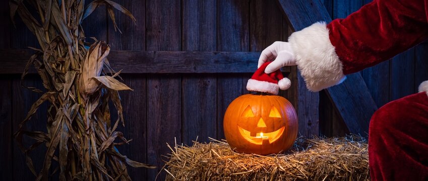 Santa claus placing a christmas hat on a glowing halloween jackolantern
