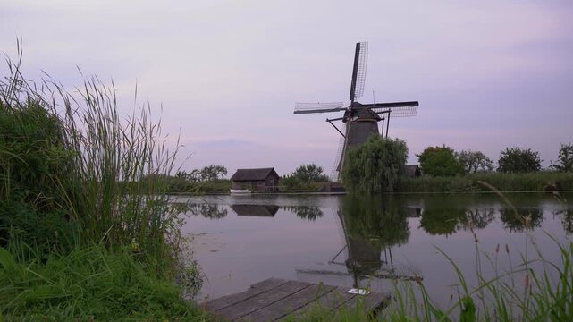 Iconic Windmill at Kinderdijk UNESCO World Heritage Site in the Netherlands, Reflecting in Calm Water on a Cloudy Summer Day.