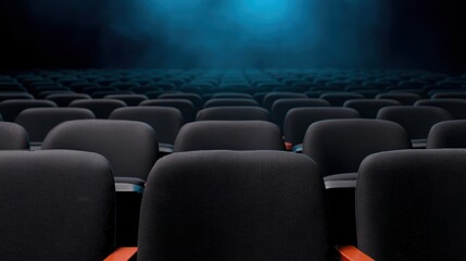 Fototapeta premium Empty black fabric seats in a theater or auditorium under dim blue lighting, arranged in neat rows facing a stage or screen.