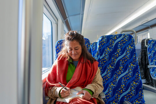 Woman writing in notebook on sunlit commuter train seat