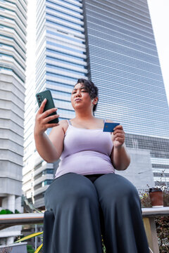 Woman using smartphone and credit card in modern city