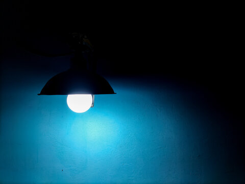 Hanging pendant lamp casting a light glow against a blue textured wall background.