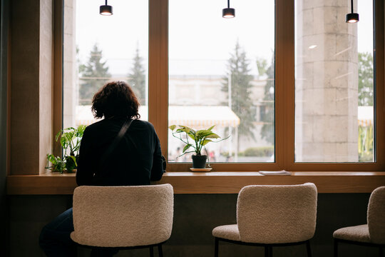 Person sitting alone by cafe window with soft daylight