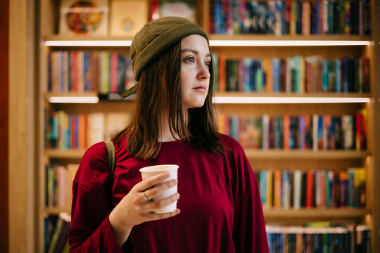 Young woman holding coffee in bookstore with bookshelves