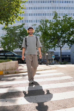 Young man with backpack crossing city street in sunlight