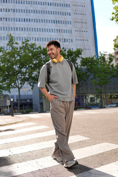 Young man crossing city street with backpack and headphones