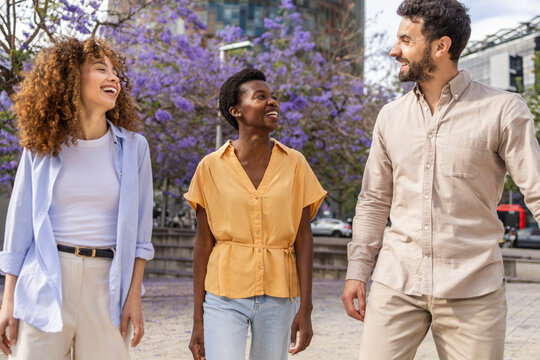Smiling friends walking in city park under purple trees