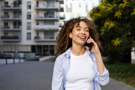 Smiling woman on phone call near modern apartment building