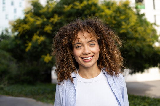 Smiling young woman with curly hair in urban park portrait