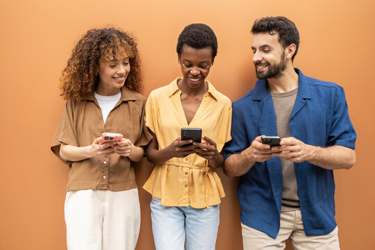 Diverse friends smiling while using smartphones together