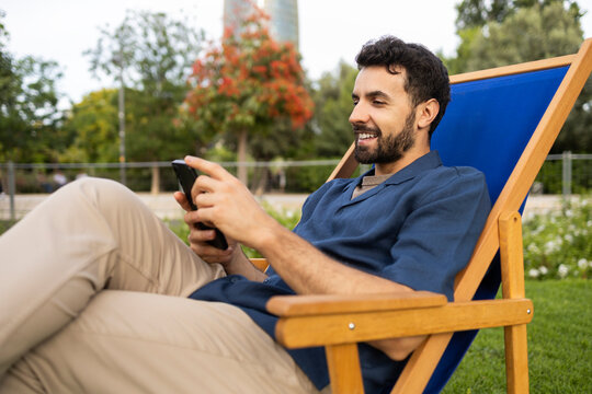 Man relaxing on deck chair using smartphone in park