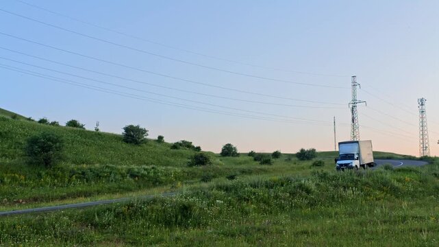 Landscape with green fields, power lines, and vehicles on a road