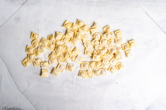 Fresh homemade ravioli pieces on floured white surface
