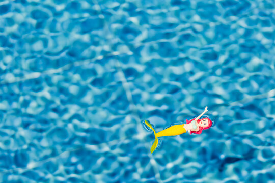 Toy mermaid floating in clear blue pool water background