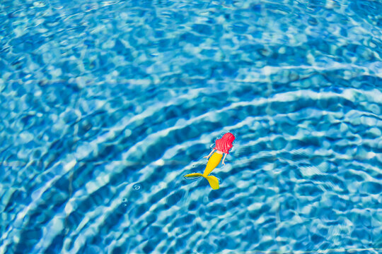 Mermaid toy floating in blue pool water with ripples