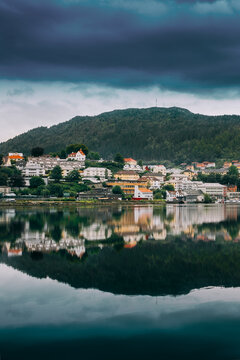Bergen, Norway. Cityscape, Residential District Near City Park. Coast Of Lake In Summer Cloudy Day. Fjellsiden Sor District Reflected In Lake Water. Coastal town reflected in the calm water of a