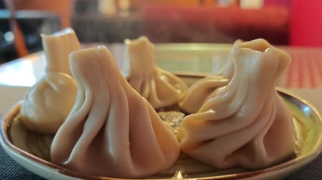 Delicious hot steaming Georgian khinkali dumplings served on a plate in a cozy restaurant with soft blurred bokeh background
