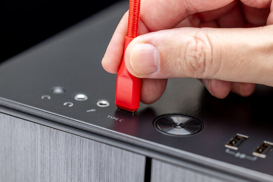 A PC user inserts a red cable into a Type-C port on the top panel of a PC system unit. The power button, USB ports, and mini-jack audio connectors are visible.