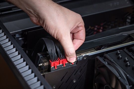 Close up of a hand connecting red modular PCI power connectors to a powerful graphics card inside a PC case. Building or upgrading a powerful gaming PC
