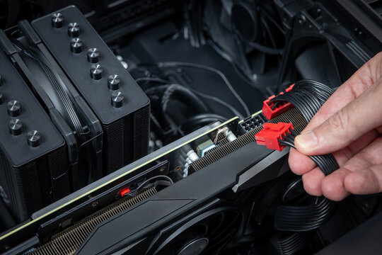 A hand connects red PCIe power connectors to a video card from above in close-up. Assembly or upgrade of a powerful gaming PC