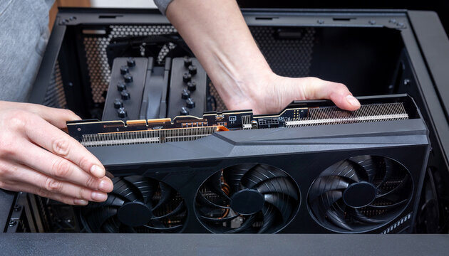 A technician installs a powerful triple-fan gaming graphics card on a gaming PC motherboard. A dual-tower CPU cooler and black power cables are visible