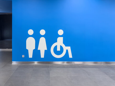 White restroom symbols for male female and wheelchair access on bright blue wall background. Clean minimalist public toilet icons for indoor navigation in modern facility space