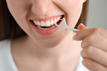 Fototapeta premium Happy young woman cleaning her teeth with dental floss pick on light grey background, closeup