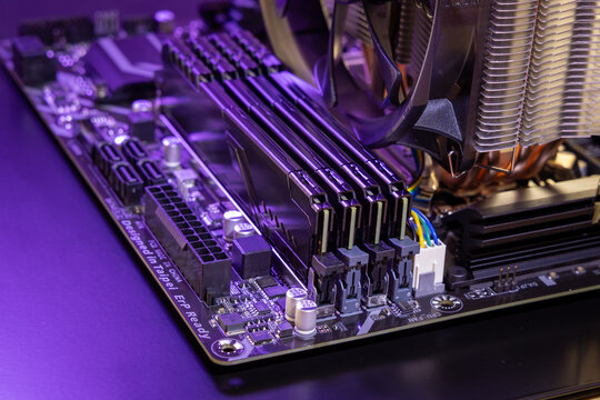 Close-up of four DDR RAM modules on a computer motherboard. CPU cooler fan, metal heatsink fins, and a power connector are visible