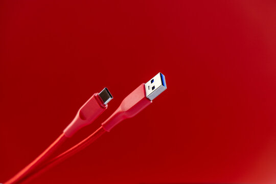Red USB cables with USB-C and USB-A connectors on a red background. Silver metal plugs. Braided cord. Equipment connection or charging cable