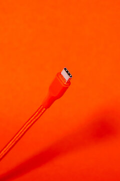 Red USB-C cable close-up on a bright orange background. Braided cord runs diagonally to a silver Type-C connector with visible contacts