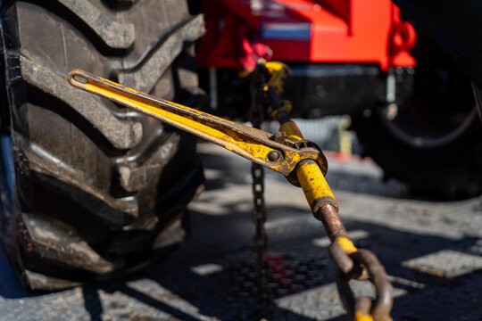 Industrial turnbuckle ratchet tensioner and yellow tie-down lever securing a tractor tire during flatbed commercial cargo transport